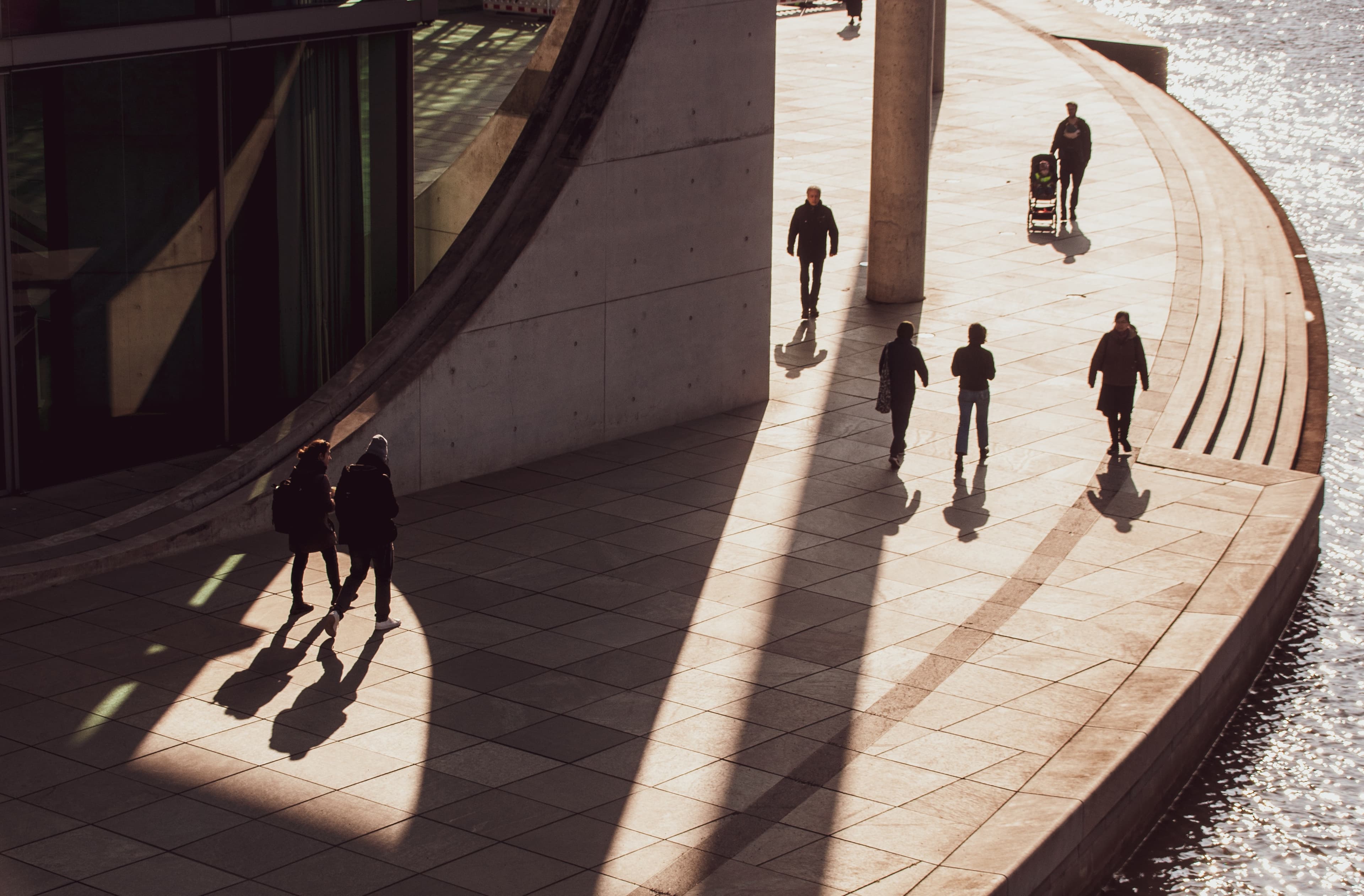 People walking along a riverside path in the sunlight