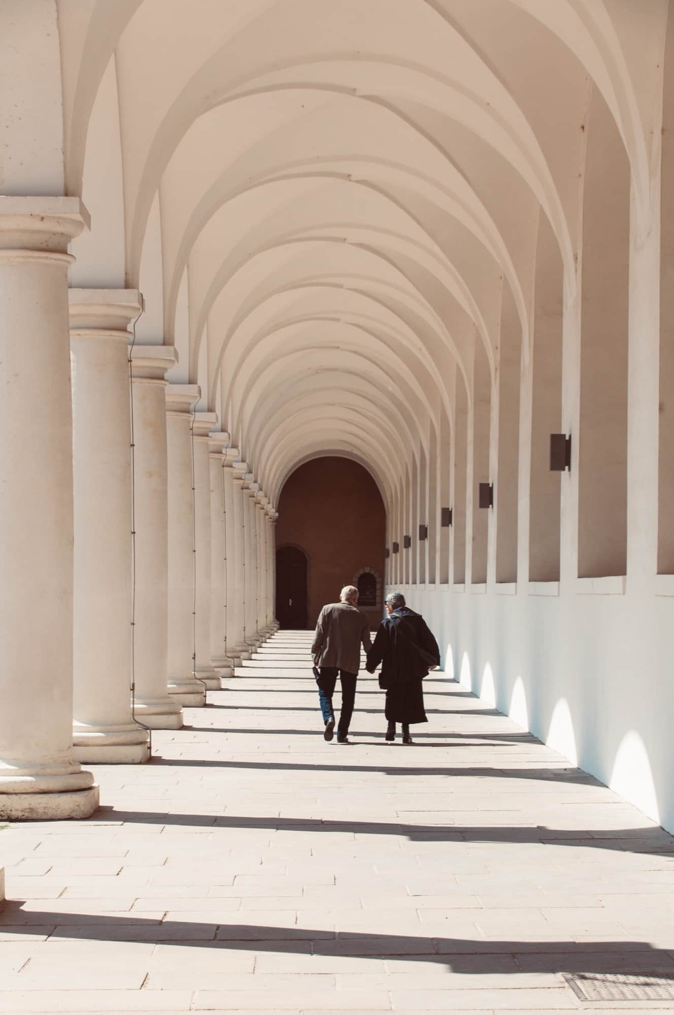 Two people walking together through a long arcade