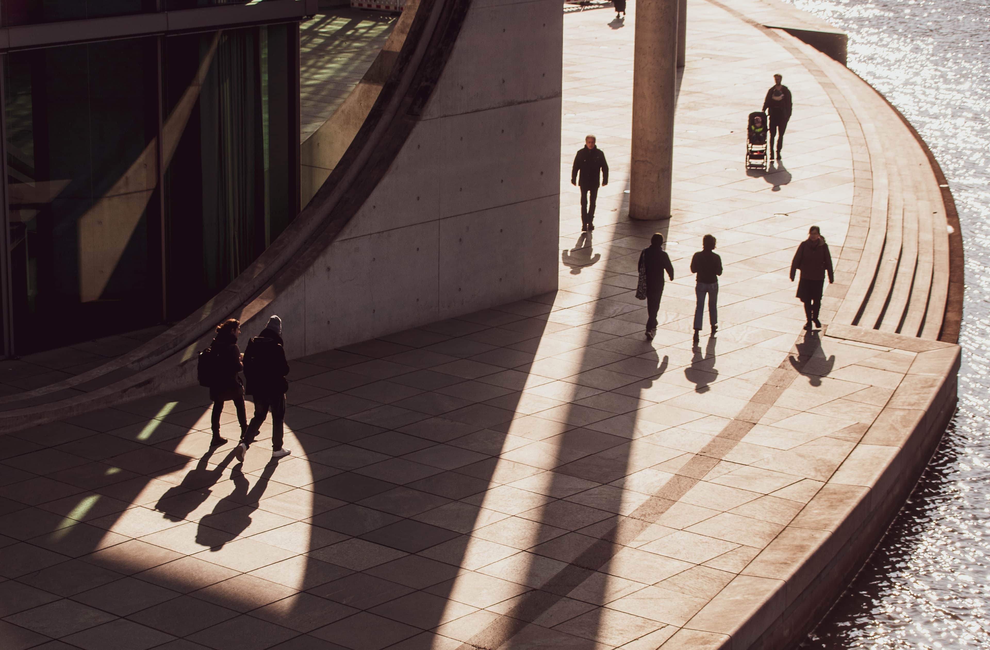 People walking along a riverside path in the sunlight